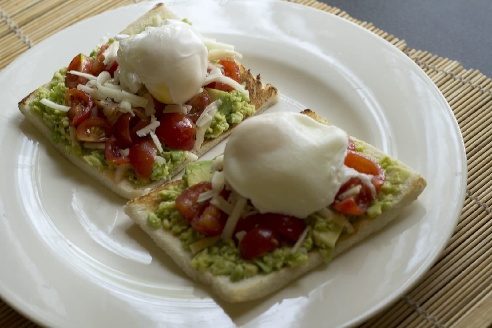 Two slices of toast with smashed avocado, cherry tomatoes, grated cheese and poached eggs