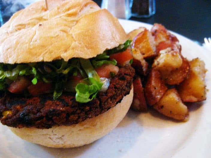 Black bean burger with lettuce and tomato in a soft bun, with roasted potatoes on the side