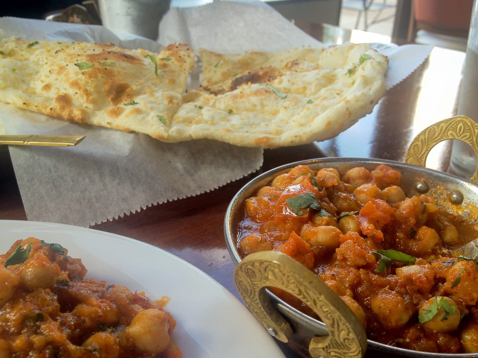 Chana masala in a brass-handled bowl with garlic naan behind