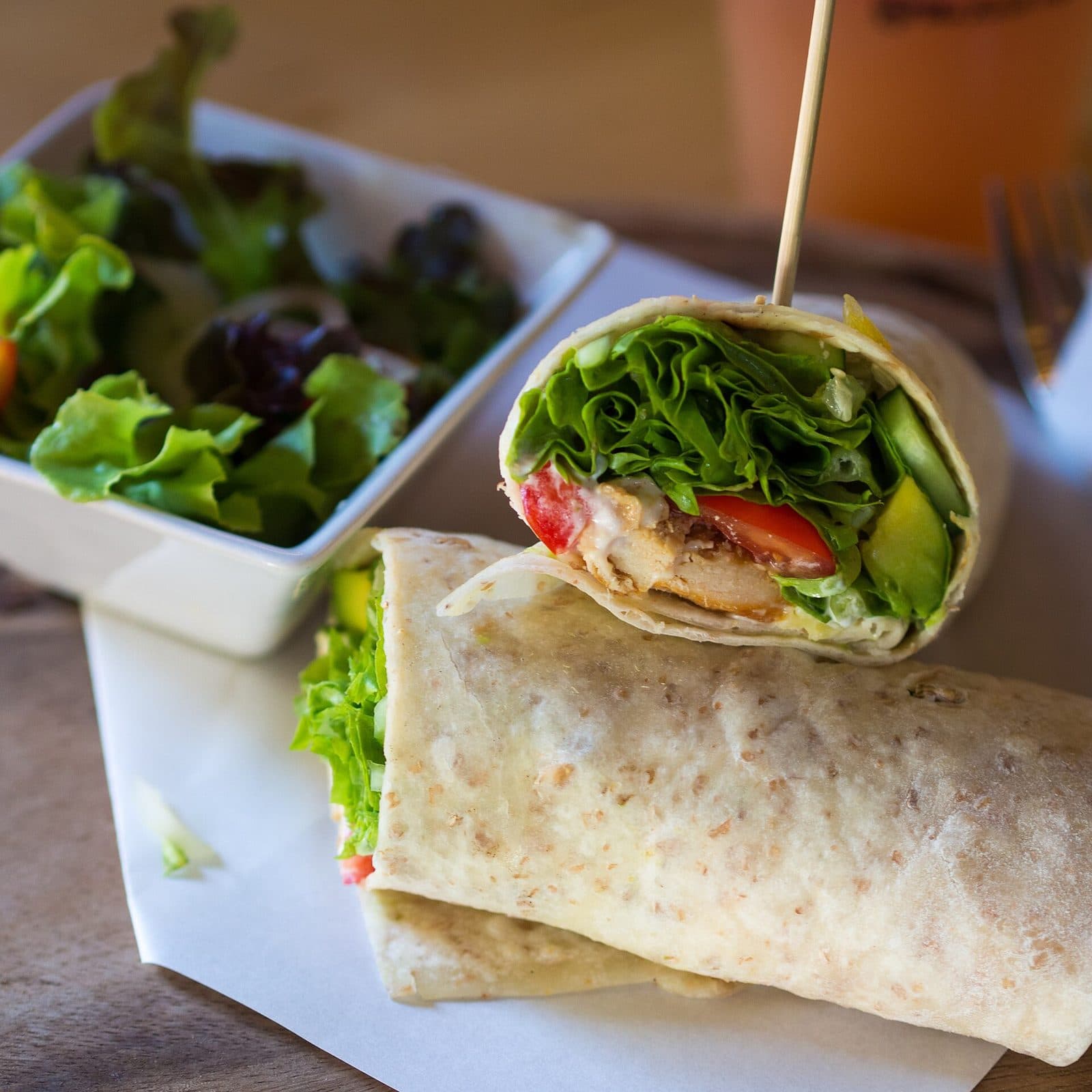 Halved chicken and avocado wrap with lettuce and tomato, served with a side salad