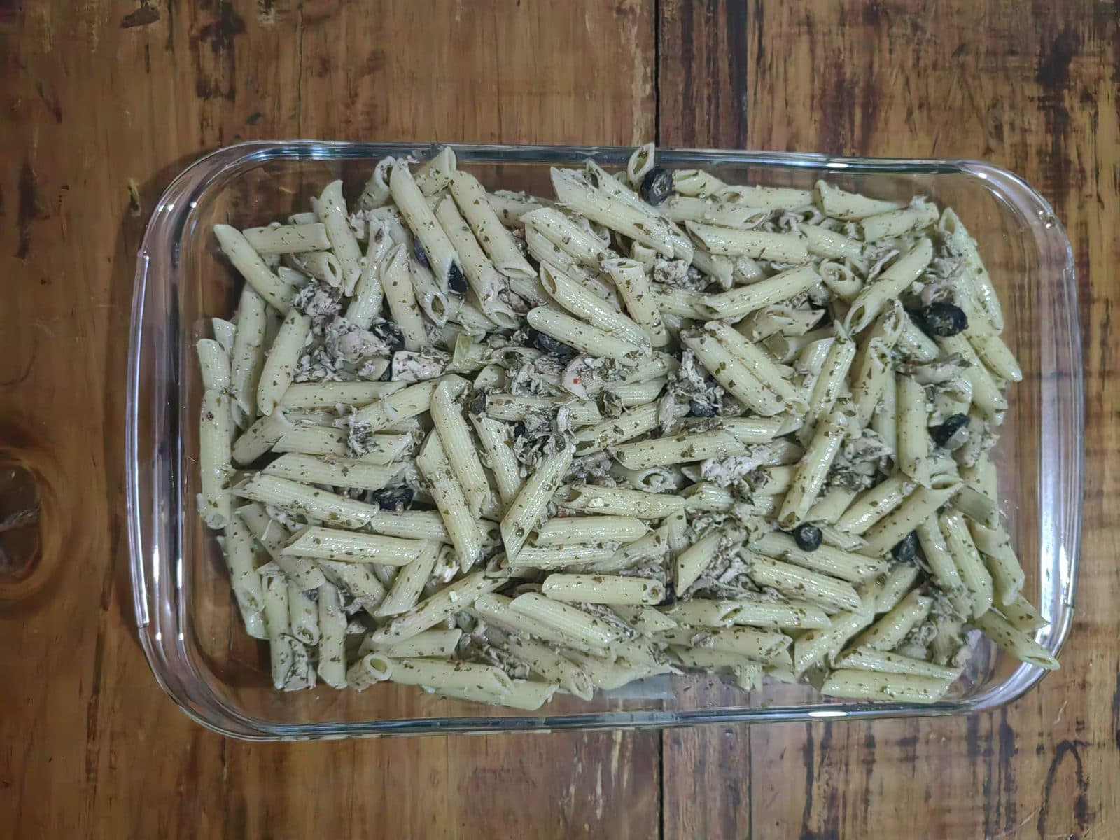 Penne tossed with basil pesto, shredded chicken and black olives in a glass baking dish, top-down