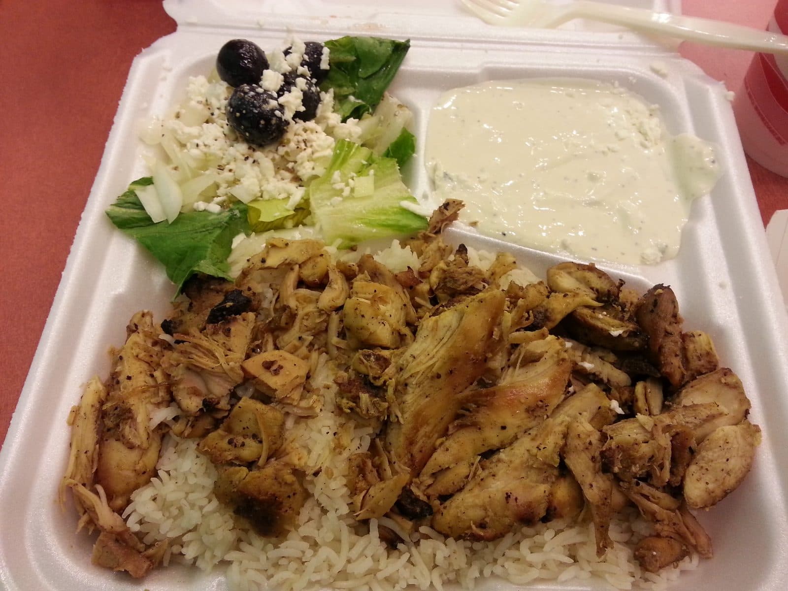 Chicken shawarma over rice with a feta-olive salad and garlic yogurt sauce in a takeaway box