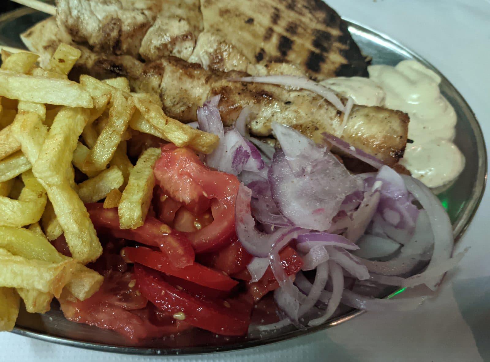 Grilled chicken souvlaki skewers with charred pitta, tomato, red onion, tzatziki and chips on a metal platter