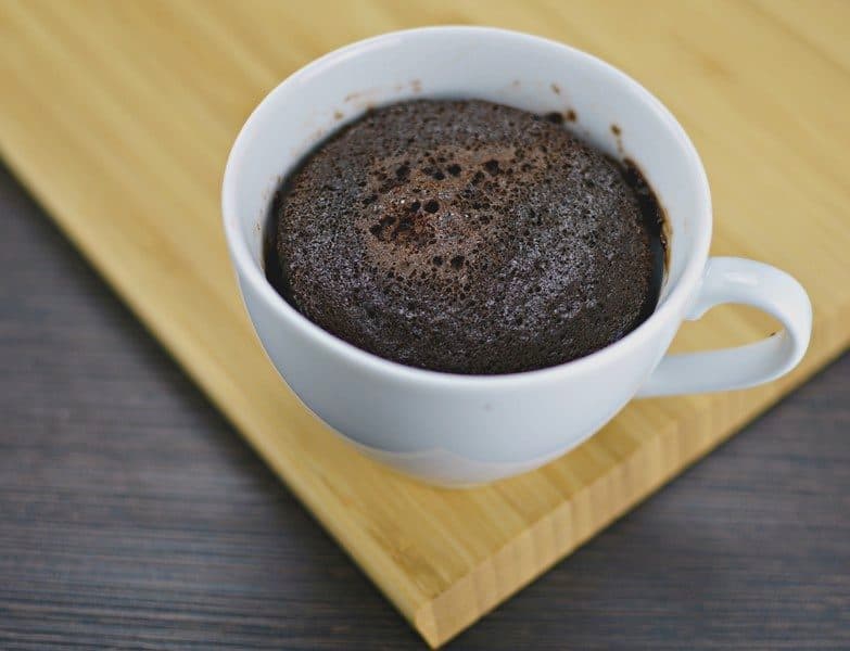 Chocolate mug cake baked in a white cup on a wooden board