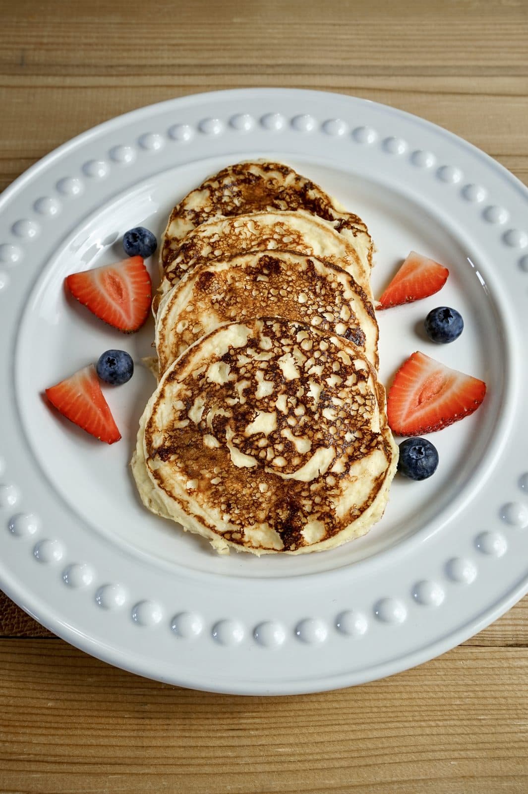 Stack of golden cottage cheese pancakes with strawberries and blueberries on a white plate