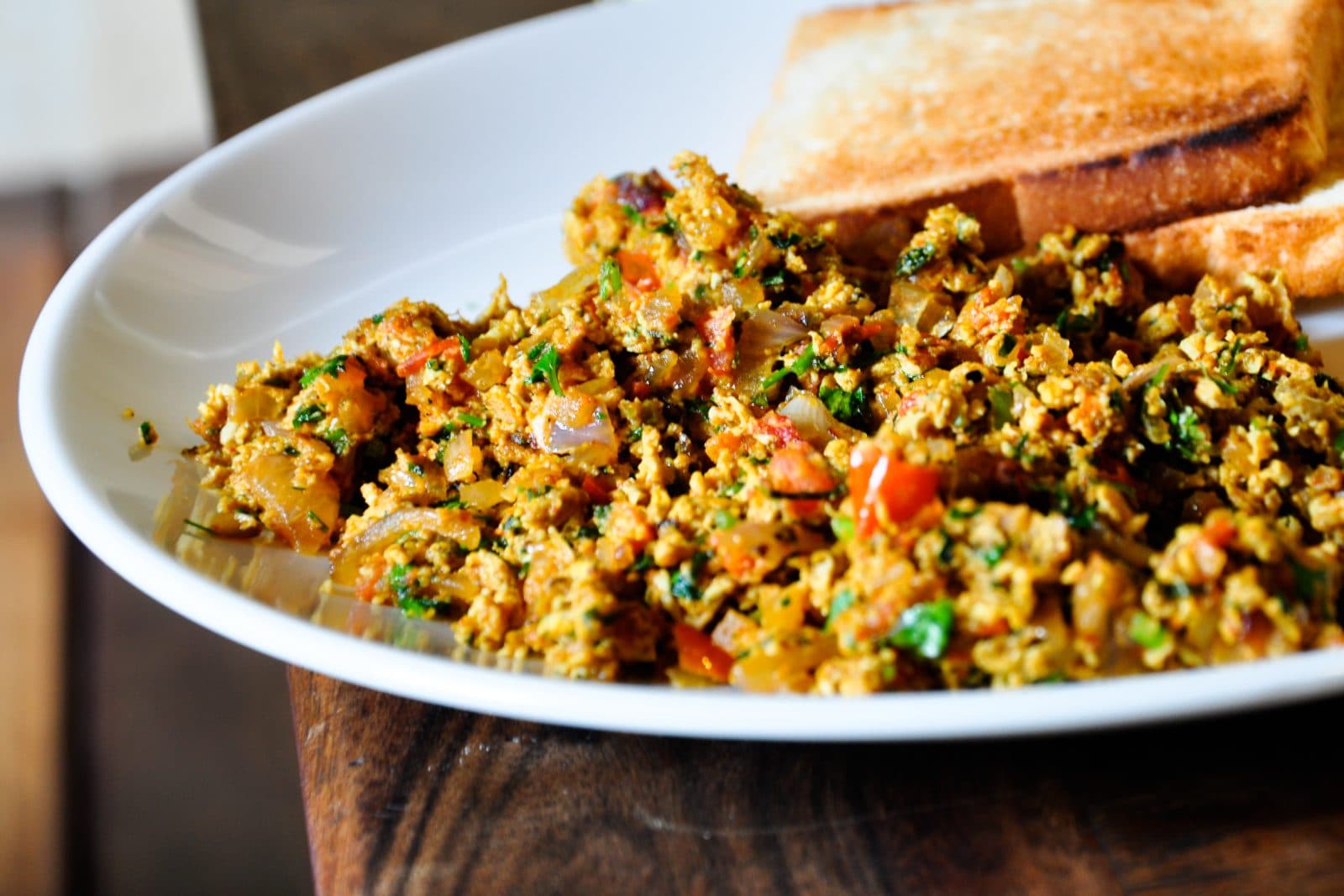 Spicy Indian egg bhurji with tomato and coriander on a white plate with toast
