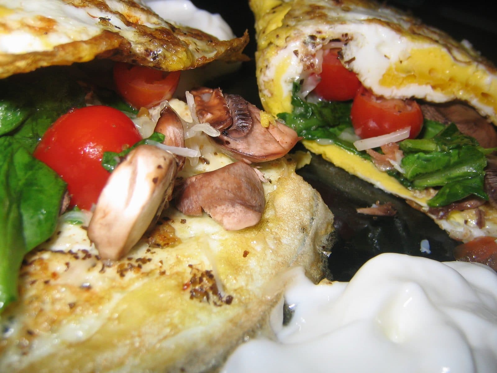Close-up of a folded omelette filled with spinach, cherry tomatoes, mushrooms and grated cheese