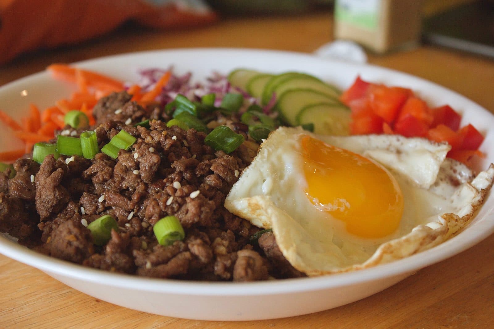 Beef bulgogi with scallions and sesame, a fried egg, cucumber, carrot, cabbage and red pepper in a bowl