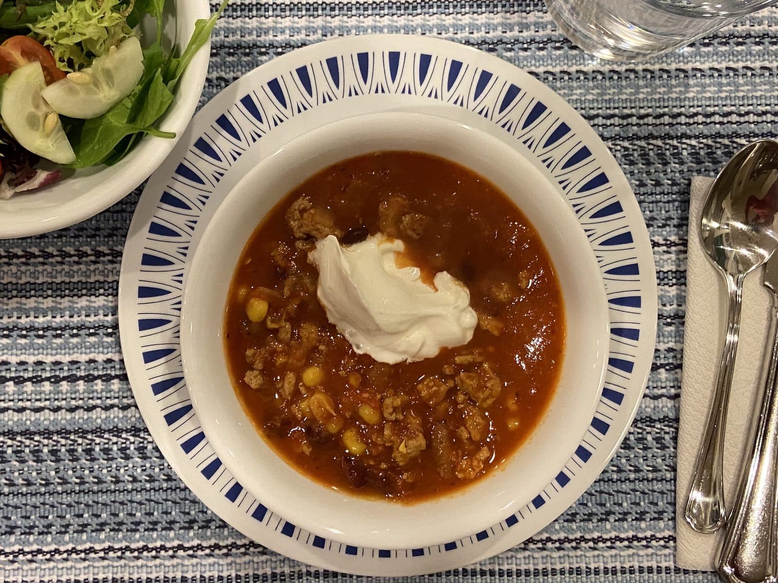 Bowl of turkey chili with beans and sweetcorn topped with a dollop of sour cream, on a blue-rimmed plate