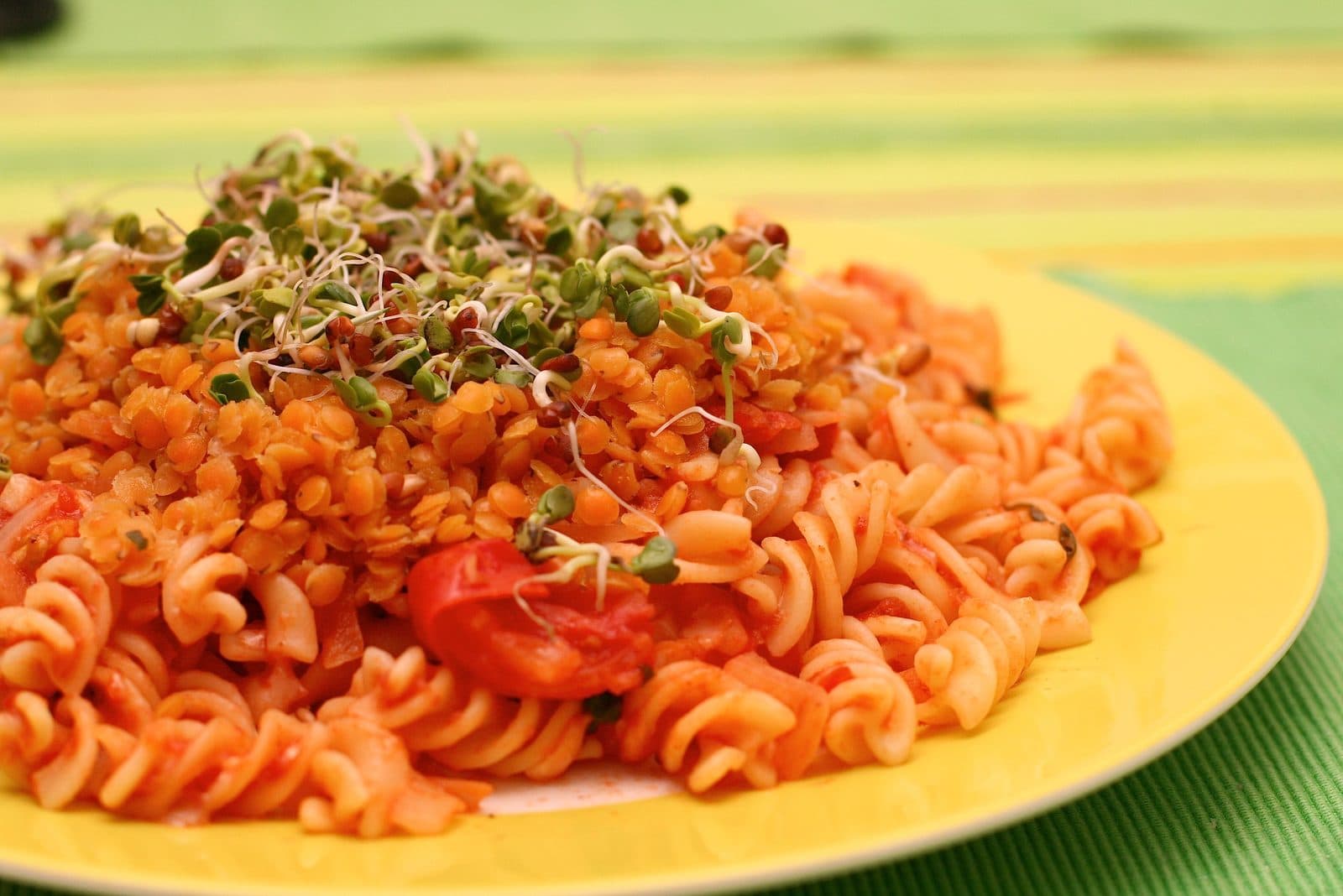 Fusilli in tomato sauce topped with red lentils and sprouts on a yellow plate