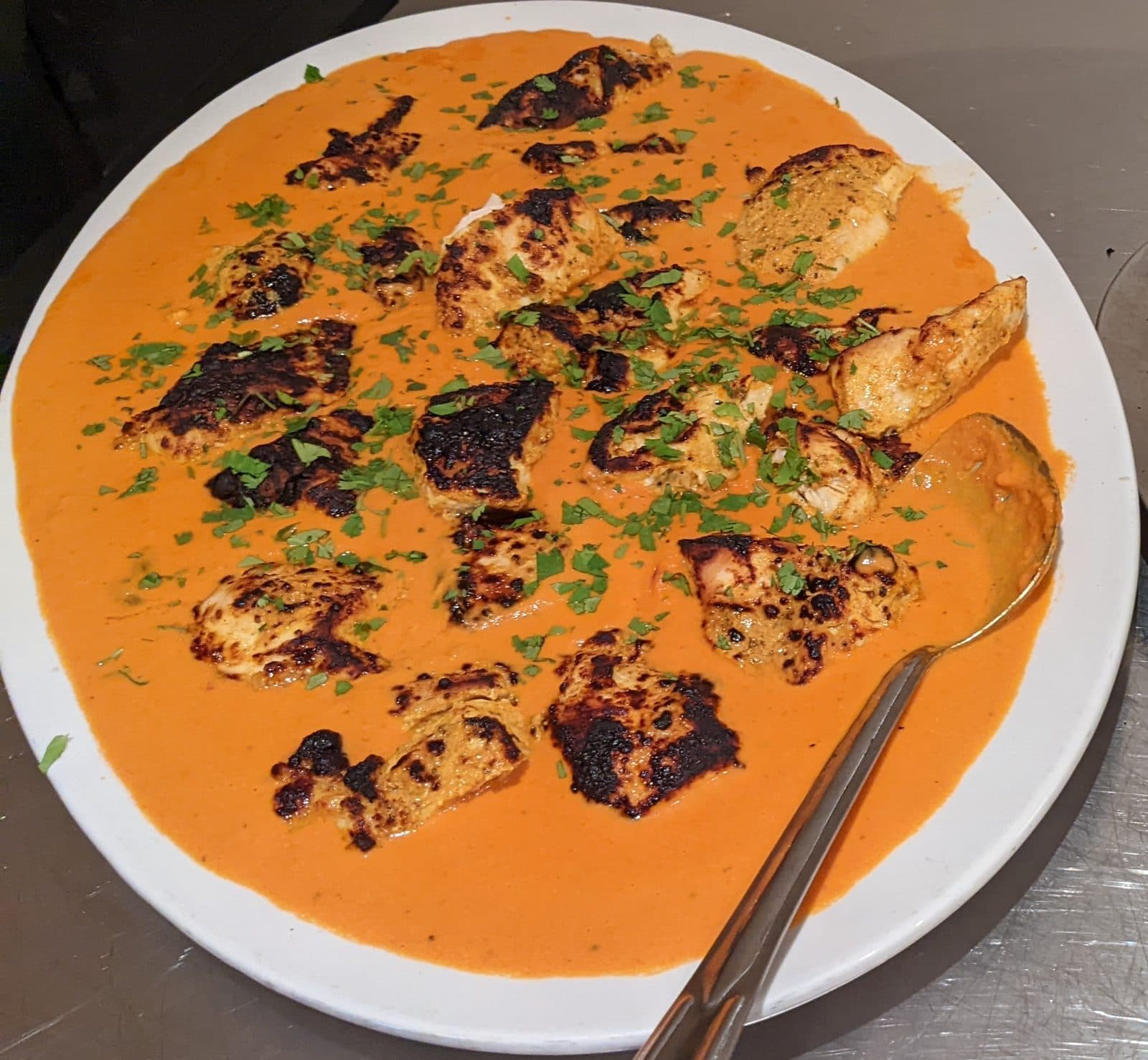 Charred chicken tikka pieces in a creamy orange masala sauce on a white platter, scattered with coriander