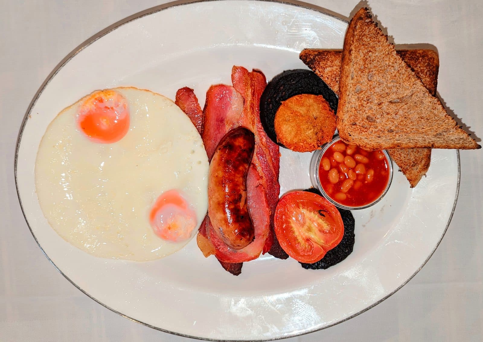 Full English breakfast: fried eggs, bacon, sausage, black pudding, hash brown, grilled tomato, beans and wholemeal toast