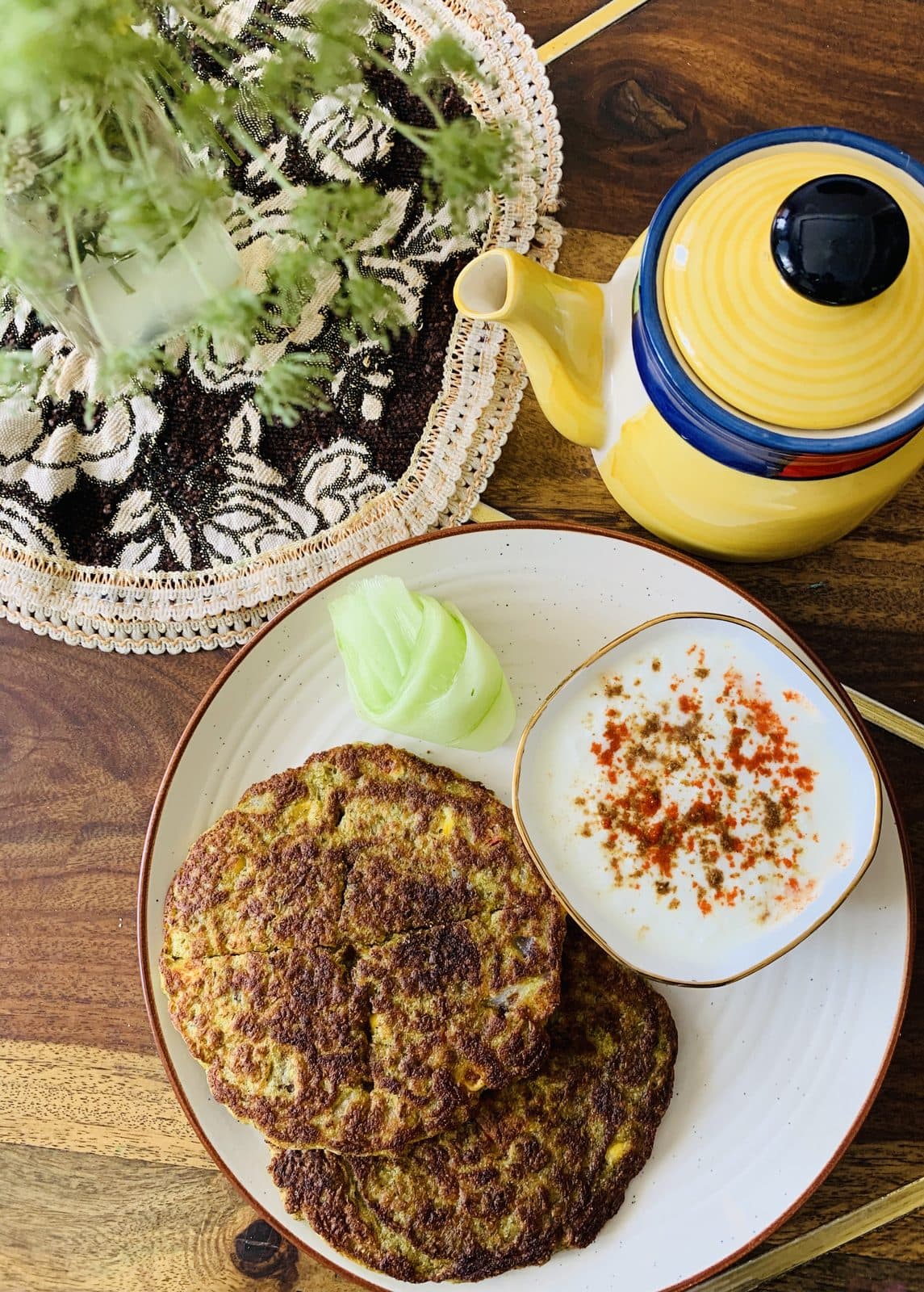 Two golden moong dal chillas on a plate with a bowl of spiced yogurt, top-down