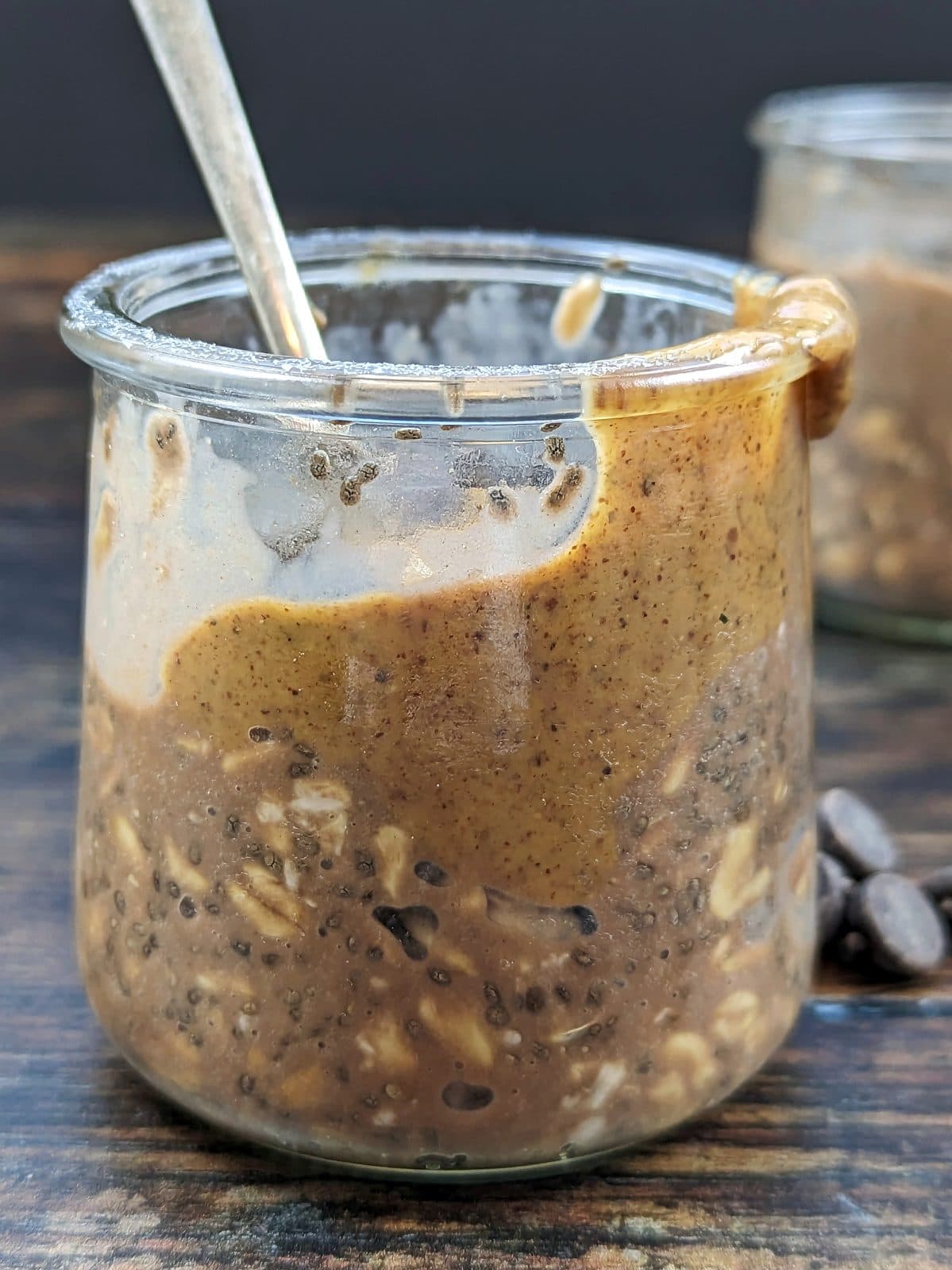 Glass jar of chocolate protein overnight oats with chia seeds and a nut-butter swirl