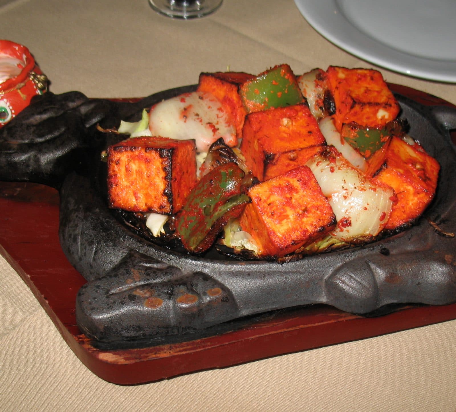 Charred paneer tikka cubes with peppers and onion on a cast-iron sizzler platter