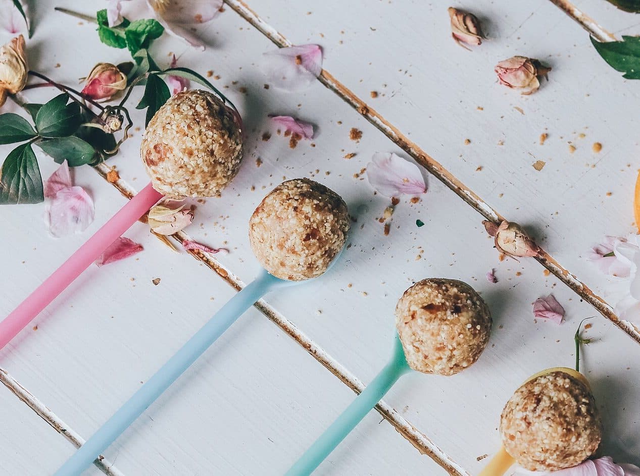 Nutty no-bake energy balls on pastel spoons on a white wooden table