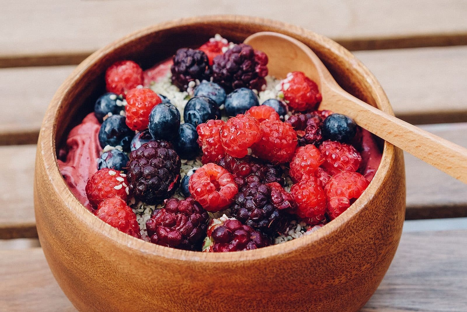 Pink berry smoothie bowl topped with raspberries, blueberries and blackberries in a wooden bowl
