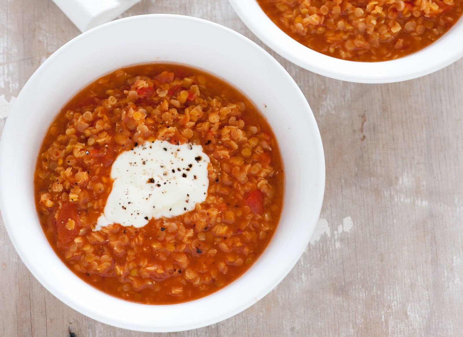 Bowl of red lentil and tomato soup topped with a dollop of yogurt and black pepper