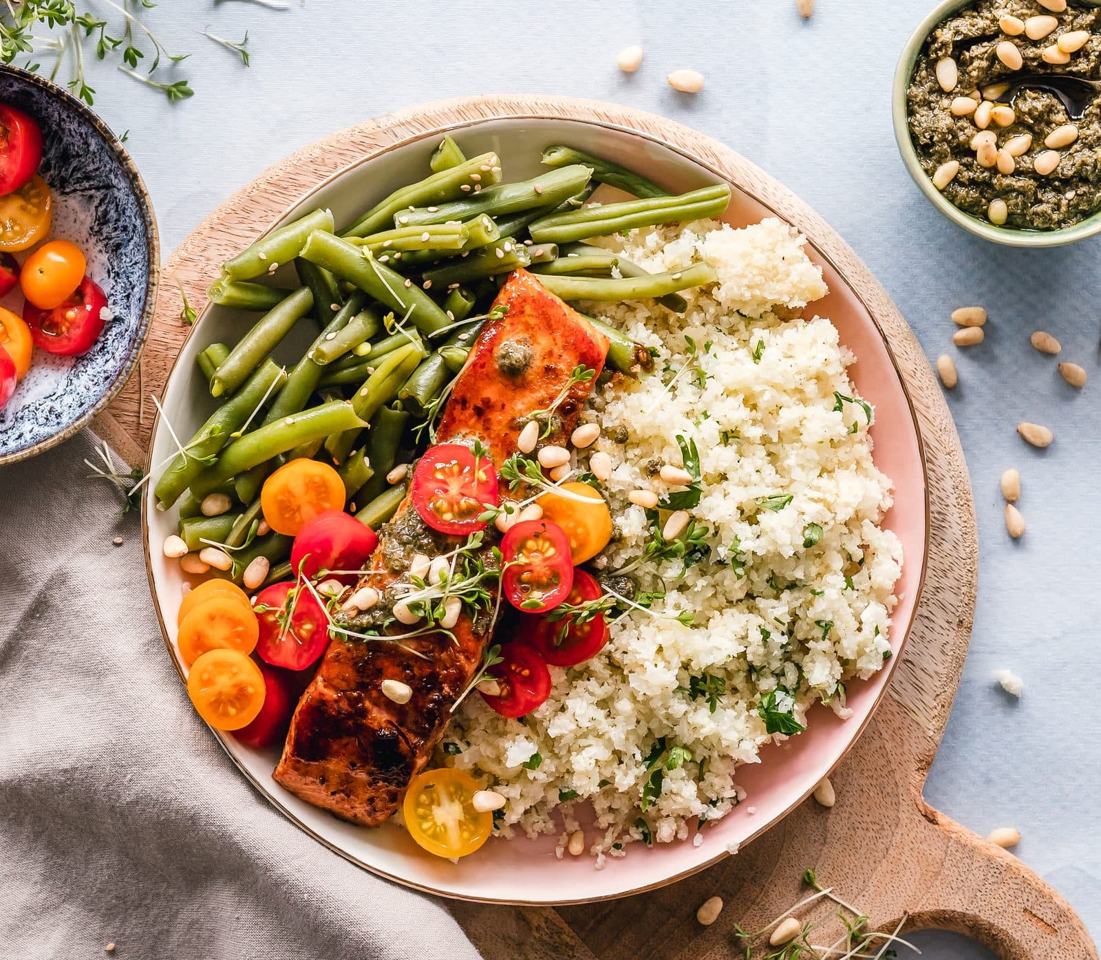Overhead view of a glazed salmon fillet in a bowl with quinoa, green beans, cherry tomatoes and pine nuts