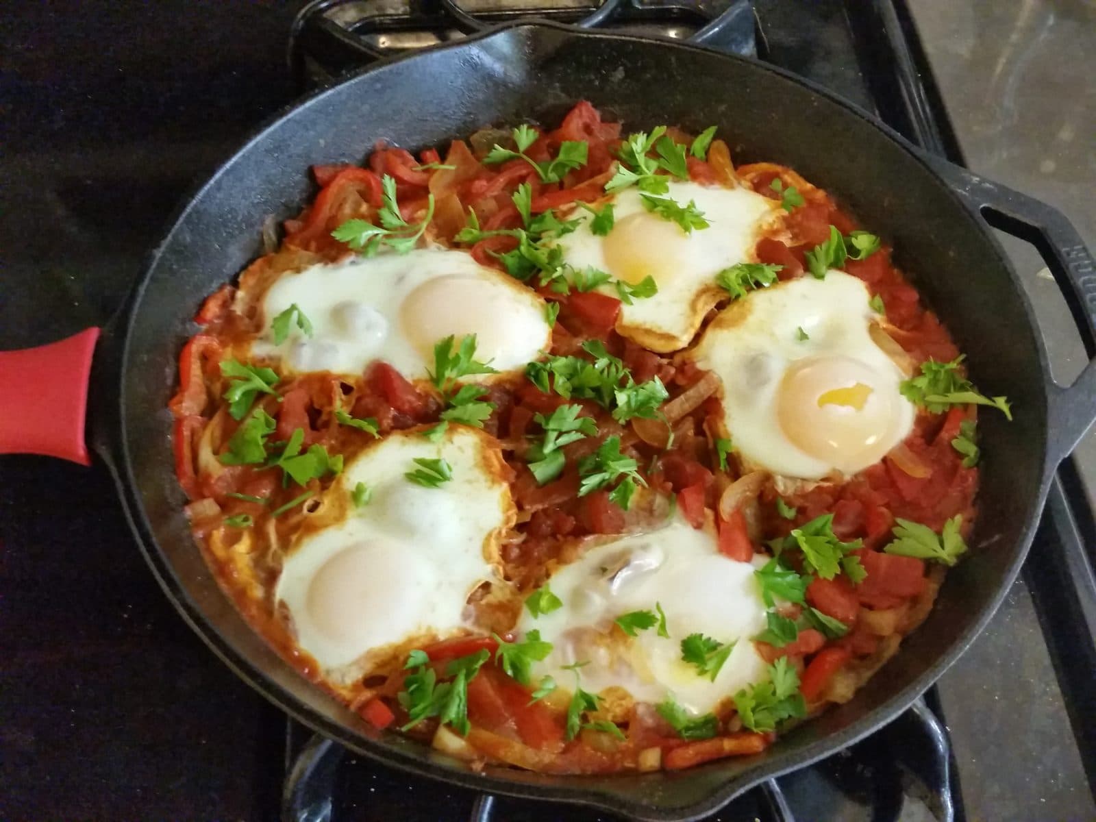Five eggs baked in a tomato and red pepper sauce in a cast-iron pan, scattered with parsley