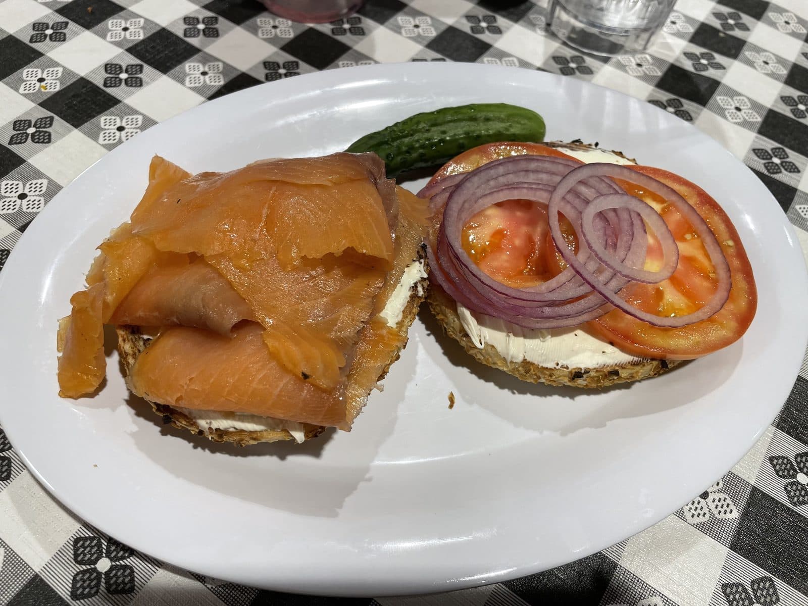 Open bagel with cream cheese, smoked salmon, tomato and red onion rings, with a pickle on the side