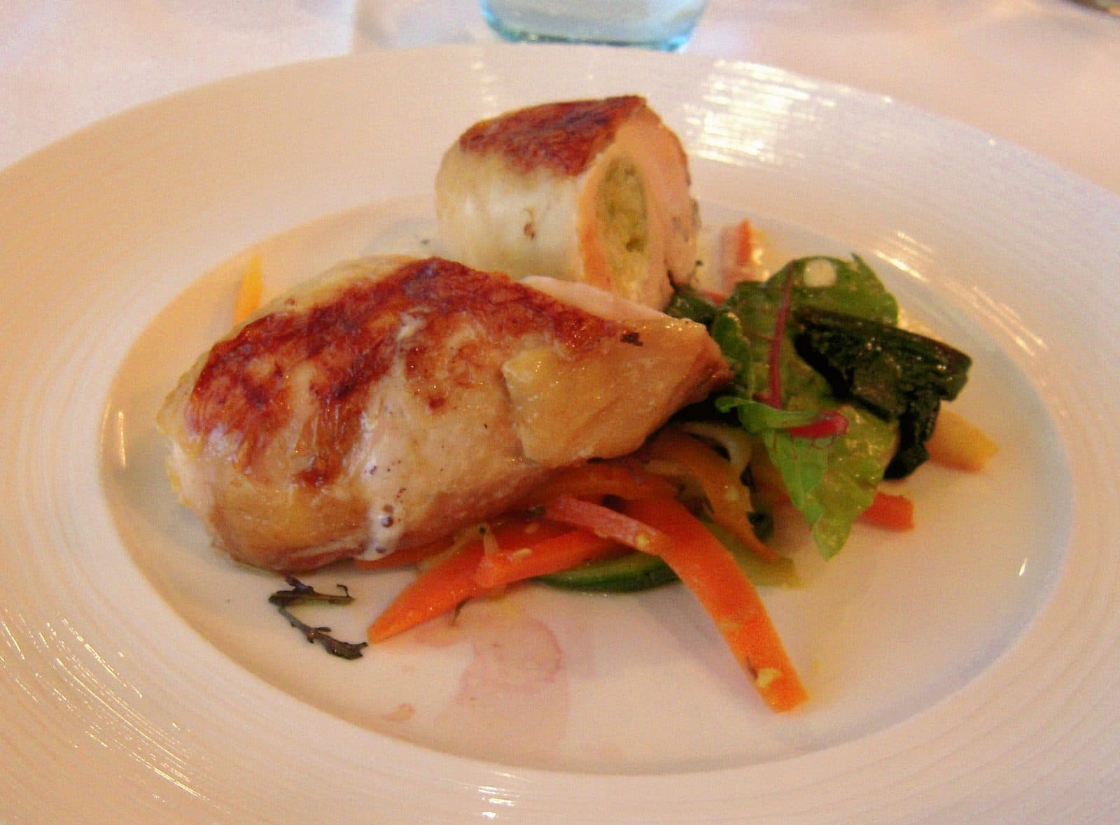 Golden roasted stuffed chicken breast, sliced to show the filling, with carrot ribbons and salad leaves
