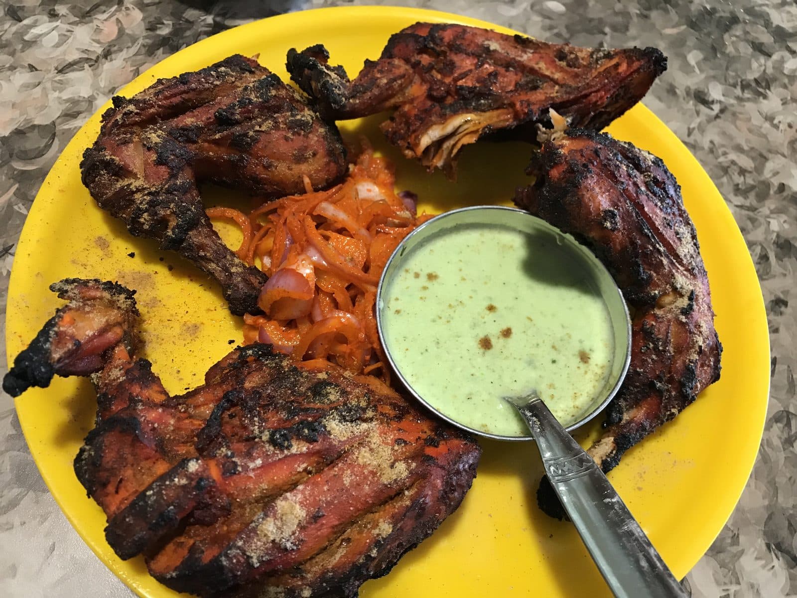 Charred tandoori chicken legs on a yellow plate with mint chutney and onion salad