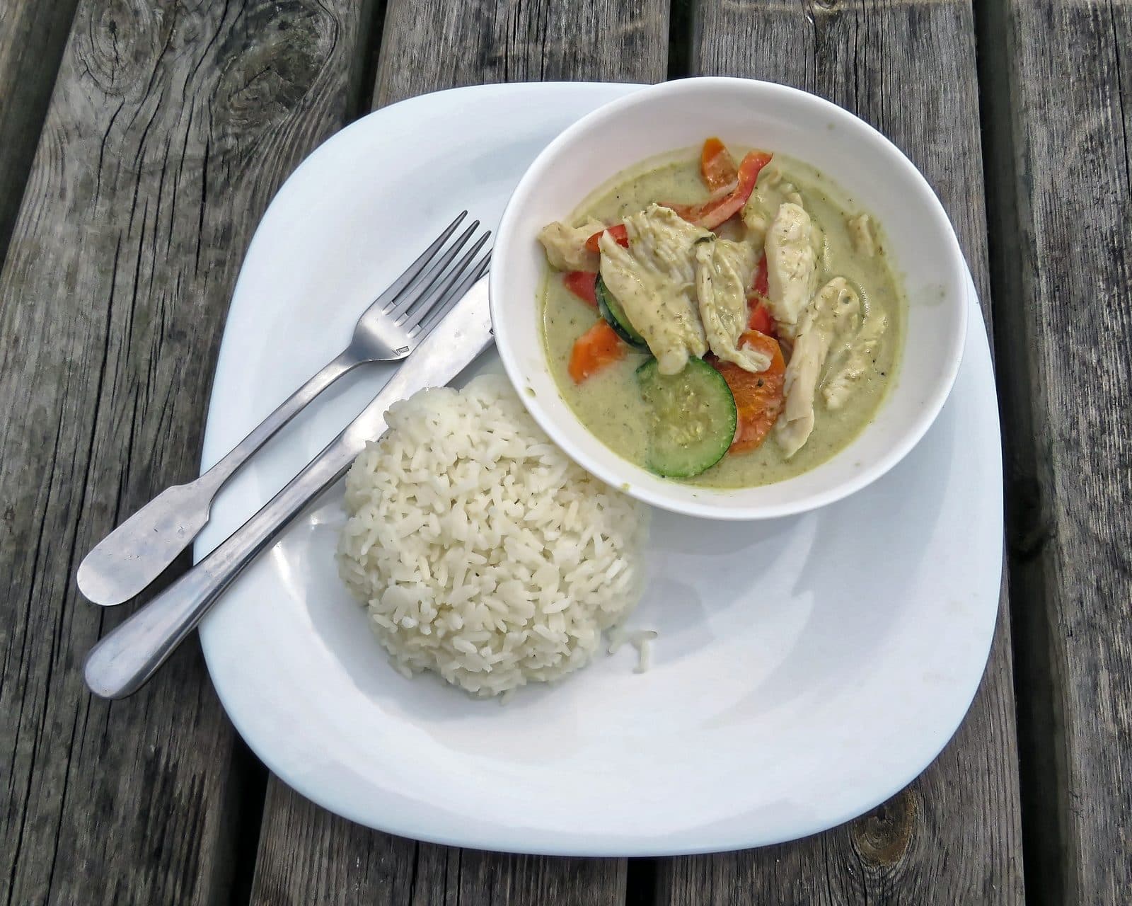 Thai green chicken curry with peppers, carrot and courgette beside a mound of rice, top-down