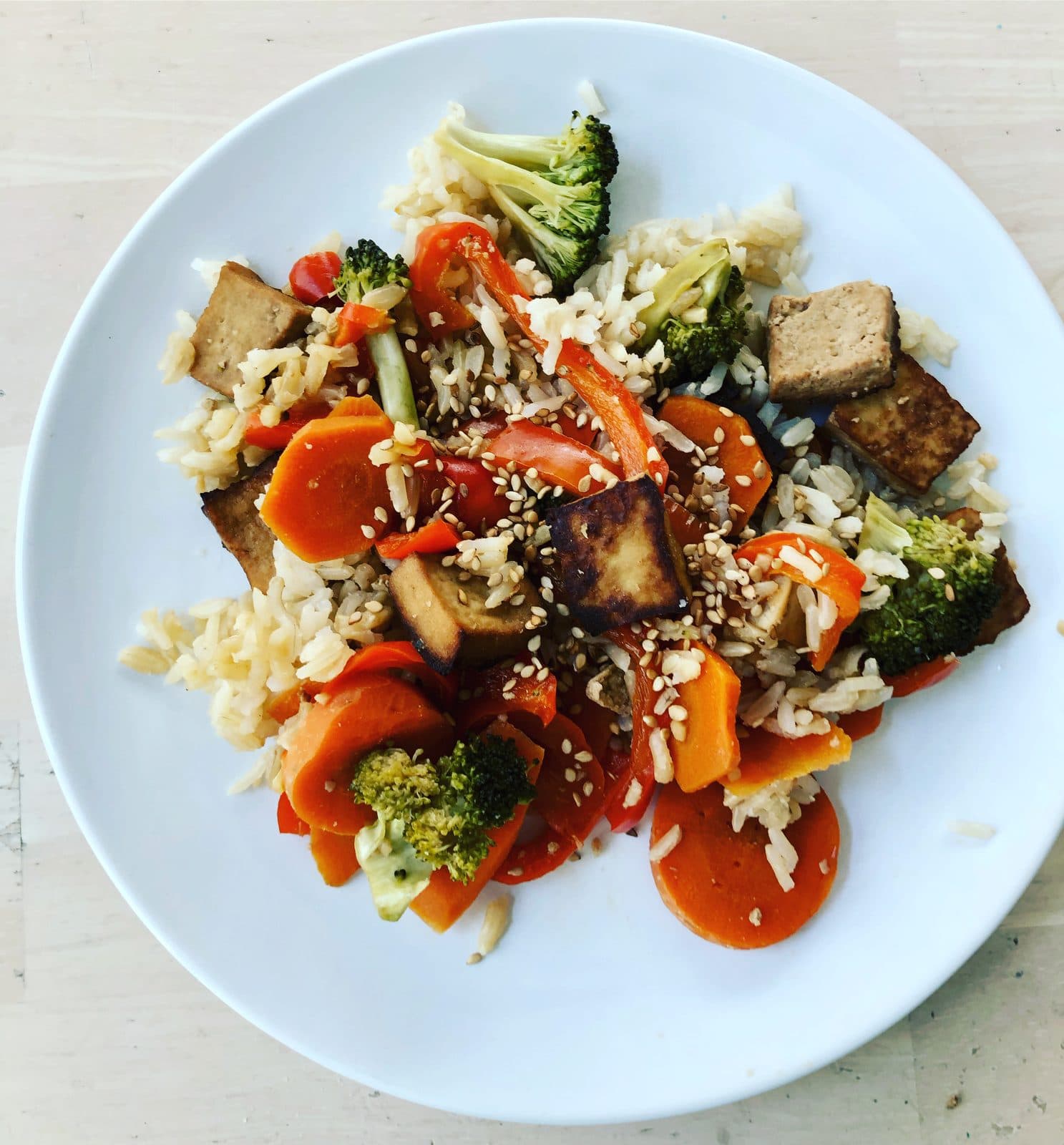 Tofu stir-fry with carrots, broccoli and red pepper over rice with sesame seeds, top-down