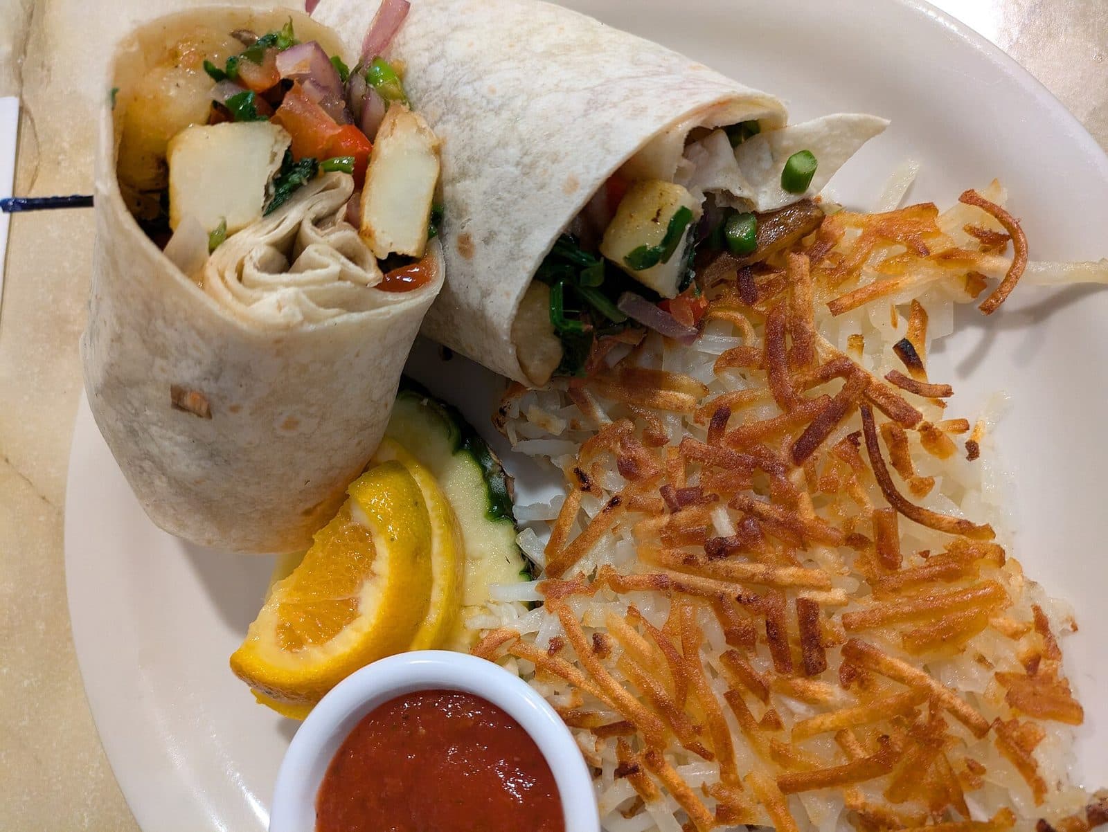 Vegan breakfast burrito cut in half, with hash browns, orange slices and salsa