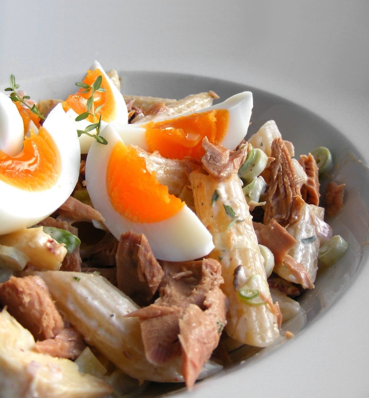 Creamy tuna penne salad with spring onion, topped with halved boiled eggs and thyme