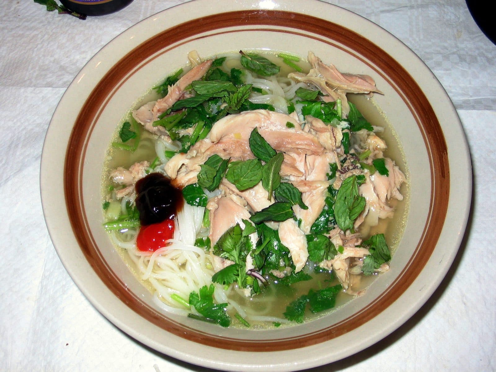 Bowl of chicken pho with rice noodles, shredded chicken, mint, coriander, chilli and hoisin